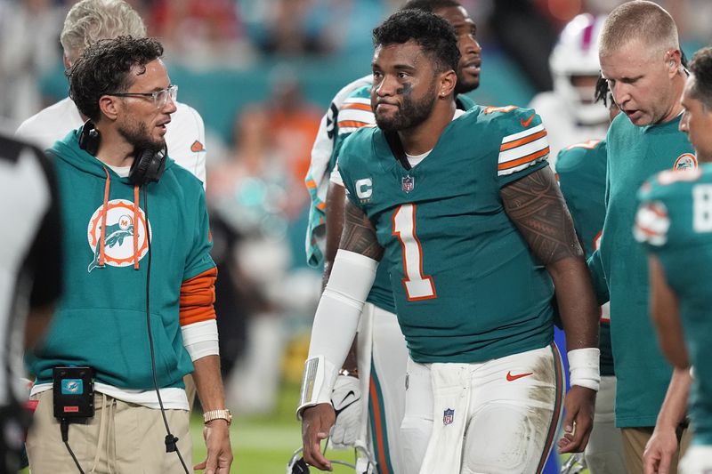 Miami Dolphins head coach Mike McDaniel talks to quarterback Tua Tagovailoa (1) as he leaves the game after suffering a concussion during the second half of an NFL football game against the Buffalo Bills, Thursday, Sept. 12, 2024, in Miami Gardens, Fla. (AP Photo/Rebecca Blackwell)