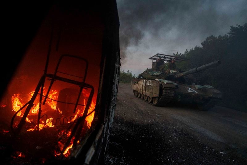 A Ukrainian tank passes by a burning car near the Russian-Ukrainian border, Sumy region, Ukraine, Wednesday, Aug. 14, 2024. (AP Photo/Evgeniy Maloletka)