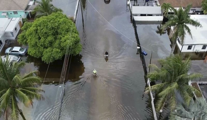 This arial view taken from video shows people walking on a flooded street in Northeast Miami-Dade County on Thursday, June 13, 2024. A tropical disturbance brought a rare flash flood emergency to much of southern Florida the day before. Floridians prepared to weather more heavy rainfall on Thursday and Friday. (AP Photo/Daniel Kozin)
