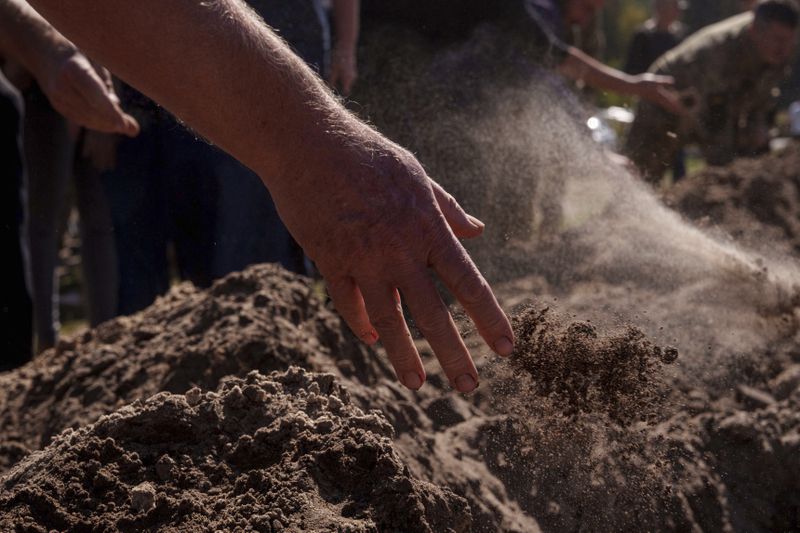 People throw three handfuls of soil into a grave during the funeral ceremony of six Ukrainian servicemen killed in a Russian rocket attack at a Ukrainian military academy, during their funeral ceremony in Poltava, Ukraine, Saturday Sept. 7, 2024. (AP Photo/Evgeniy Maloletka)