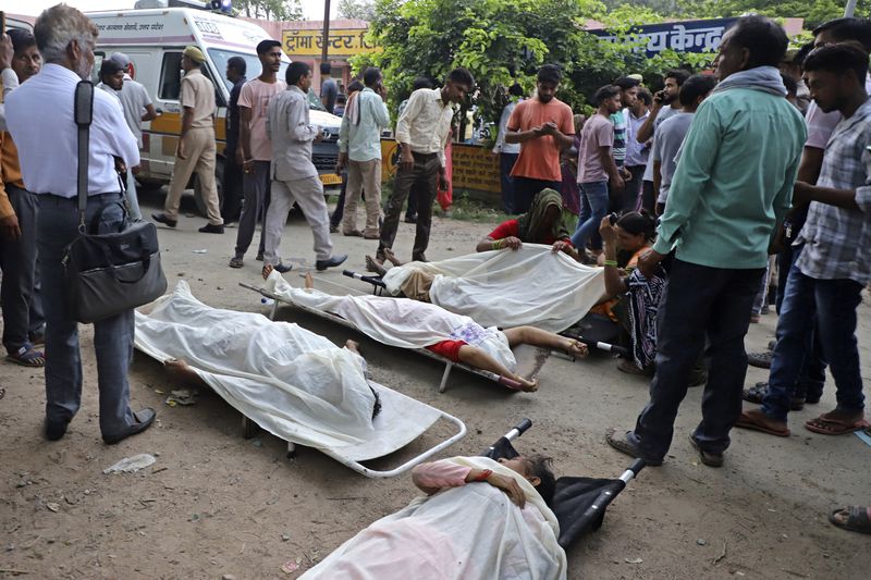 People stand around the bodies lying covered on stretchers outside the Sikandrarao hospital in Hathras district about 350 kilometers (217 miles) southwest of Lucknow, India, Tuesday, July 2, 2024. A stampede among thousands of people at a religious gathering in northern India has killed at least 105 and left scores injured, officials said Tuesday, with many women and children among the dead. (AP Photo/Manoj Aligadi)