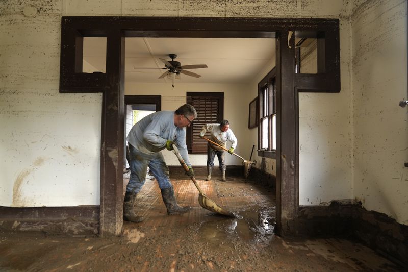 Ben Phillips, left, and his wife Becca Phillips scrape mud out of the living room of their home left in the wake of Hurricane Helene, Tuesday, Oct. 1, 2024, in Marshall, N.C. (AP Photo/Jeff Roberson)