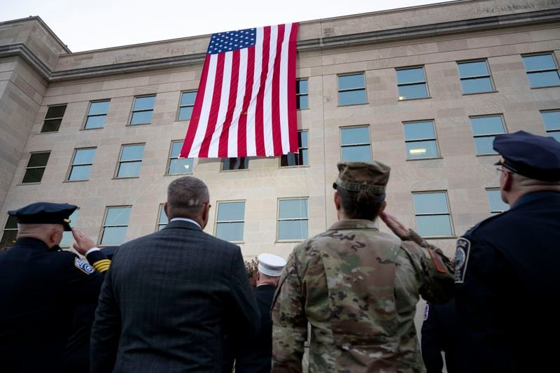 Members of the military and first responders salute as a flag in unfurled from the top of the Pentagon during a dawn Sept. 11th remembrance ceremony on Wednesday, Sept. 11, 2024 in Washington. (AP Photo/Kevin Wolf)