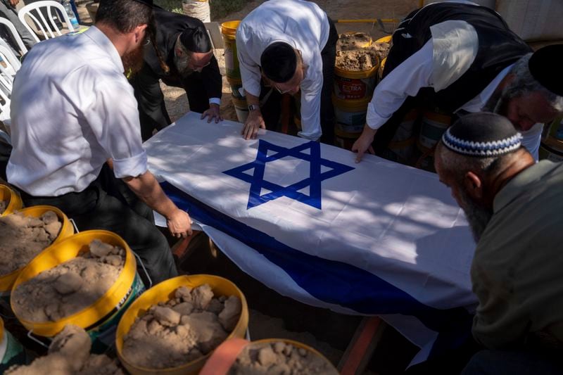 Workers from "Hevra Kadisha" lower the coffin of Avraham Munder, who was killed in Hamas captivity in the Gaza Strip and recovered by the Israeli military in Gaza, during his funeral at a cemetery of the Kibbutz Nir Oz southern Israel, Wednesday, Aug. 21, 2024. On Tuesday, the Israeli military said its forces recovered six bodies of hostages kidnapped on Oct. 7 in an overnight operation in southern Gaza. (AP Photo/Ohad Zwigenberg)