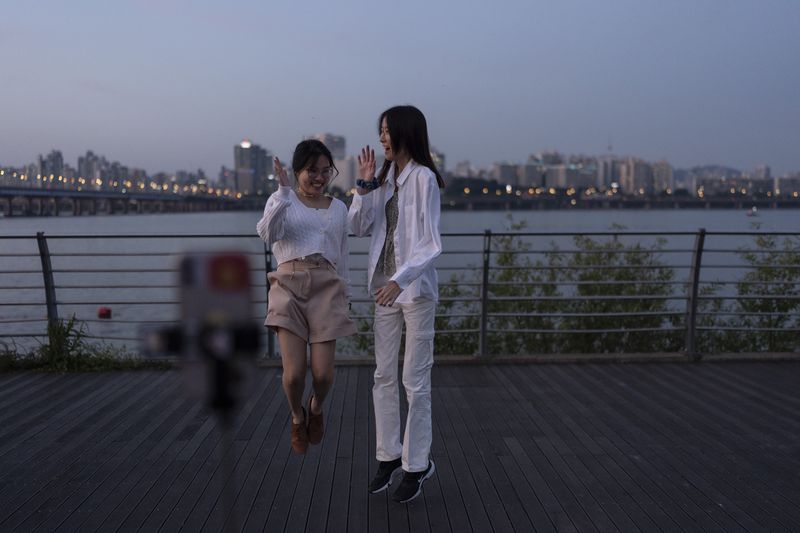 Two tourists jump together as they pose for photos with the Han River in the background at Yeouido Hangang Park, a popular spot for both residents and visitors, as dusk falls over Seoul, Wednesday, May 22, 2024. (AP Photo/Jae C. Hong)