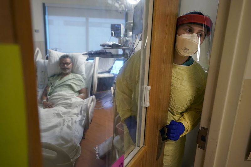 FILE - Registered nurse Rachel Chamberlin, of Cornish, N.H., right, steps out of an isolation room where where Fred Rutherford, of Claremont, N.H., left, recovers from COVID-19 at Dartmouth-Hitchcock Medical Center, in Lebanon, N.H., Monday, Jan. 3, 2022. (AP Photo/Steven Senne, File)