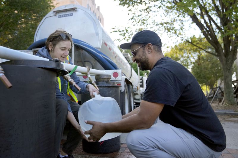 Reginald Klemz, right, fills a container of fresh water from a tanker with the help of volunteer Julie Koenke in the aftermath of Hurricane Helene Wednesday, Oct. 2, 2024, in Asheville, N.C. (AP Photo/Jeff Roberson)