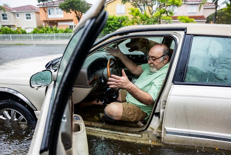 Mike Viesel and his fog Humi, wait in his flooded car for a tow truck after their car stalled out on Taft Street due to heavy rain flooding the neighborhood on Wednesday, June 12, 2024, in Hollywood, Fla. The annual rainy season has arrived with a wallop in much of Florida, where a disorganized disturbance of tropical weather from the Gulf of Mexico has caused street flooding and triggered tornado watches but so far has not caused major damage or injuries. (Matias J. Ocner/Miami Herald via AP)