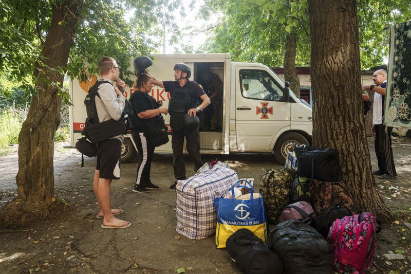 A Fenix team rescue worker places a helmet on Maryna Scherbyna as she and her children are evacuated as local people are moved from Selidove to safe areas, in Pokrovsk, Donetsk region, Ukraine, on Tuesday, Aug. 20, 2024. (AP Photo/Evgeniy Maloletka)