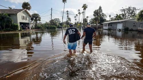 Thomas Chaves, left, and Vinny Almeida walk through floodwaters from Hurricane Helene in an attempt to reach Chaves's mother's house in the Shore Acres neighborhood Friday, Sept. 27, 2024, in St. Petersburg, Fla. (AP Photo/Mike Carlson)