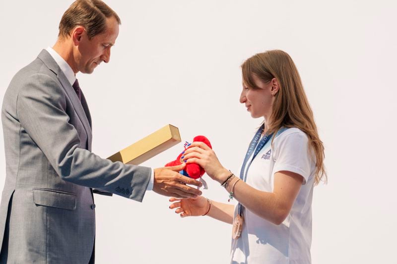 Mihai Covaliu, President of the Romanian Olympic and Sports Committee offers the Olympic games mascot to Romanian gymnast Ana Barbosu after she received the bronze medal for her women's artistic gymnastics individual floor performance at the Paris 2024 Olympics, during a ceremony, in Bucharest, Romania, Friday, Aug. 16, 2024. American gymnast Jordan Chiles called an arbitration panel's decision that dropped her out of the bronze medal position in the floor exercise at the Paris Olympics "unjust" and a "significant blow" in a message posted on social media Thursday. (AP Photo/Vadim Ghirda)