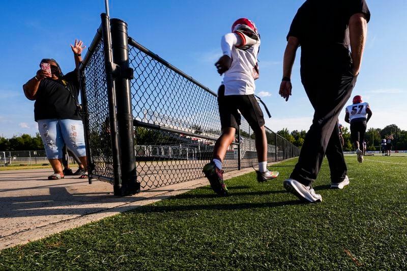 Families wave and take photos as members of the Clinton High School freshman football team arrive for a game at Brandon High in Brandon, Miss., Tuesday, Aug. 27, 2024. (AP Photo/Gerald Herbert)