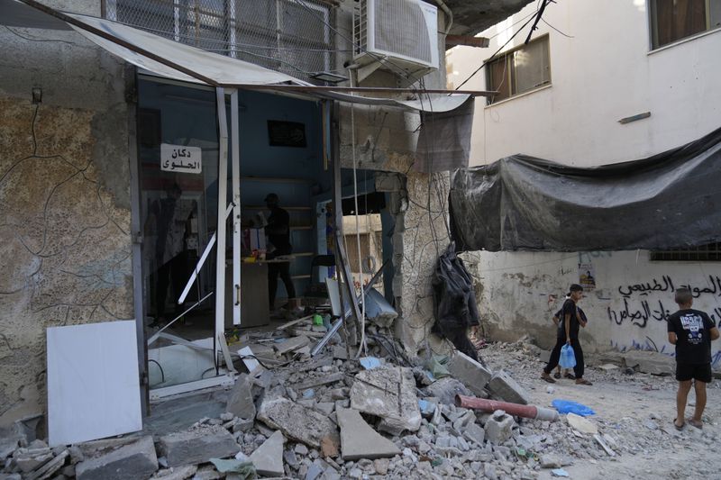 Palestinian refugees walk past rubble of a partly destroyed shop in the West Bank refugee camp of Tulkarem, Thursday, Sept. 12, 2024. (AP Photo/Nasser Nasser)