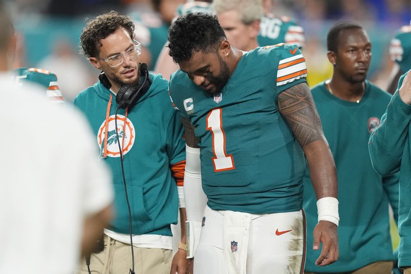 Miami Dolphins head coach Mike McDaniel talks to quarterback Tua Tagovailoa (1) as he leaves the game after suffering a concussion during the second half of an NFL football game against the Buffalo Bills, Thursday, Sept. 12, 2024, in Miami Gardens, Fla. (AP Photo/Rebecca Blackwell)