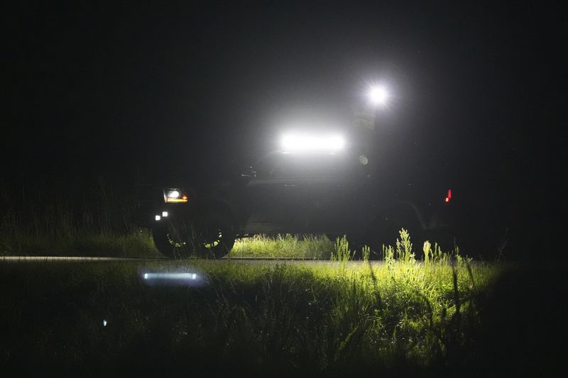 Python hunters shine their lights along a levy searching for invasive Burmese pythons, Tuesday, Aug. 13, 2024, in the Florida Everglades. (AP Photo/Wilfredo Lee)