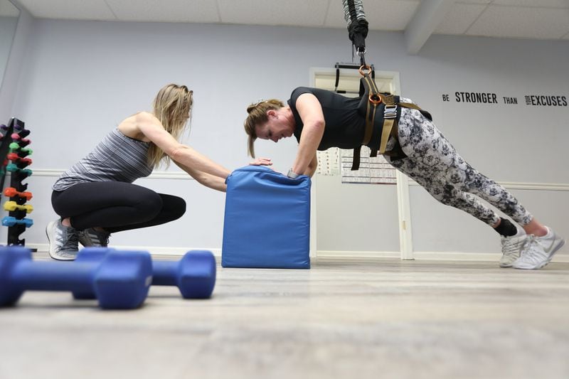 Janet Paulsen does a series of pushups with the assistance of her coach Aleksandra Kazmierczak at Studio Bungee on Feb. 19, 2020, in Marietta. MIGUEL MARTINEZ / FOR THE AJC