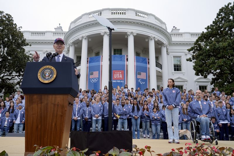 President Joe Biden, from left, speaks as Olympic swimmer Torri Huske and Paralympian basketball players Paul Schulte listen during at an event celebrating the 2024 U.S. Olympic and Paralympic teams on the South Lawn of the White House in Washington, Monday, Sept. 30, 2024. (AP Photo/Susan Walsh)