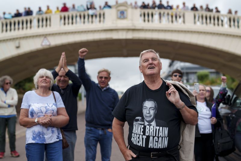 People react to Nigel Farage, leader of the Reform UK party, speaking during an electoral rally at Clacton Pier in Clacton-on-Sea, England, Wednesday, July 3, 2024. United Kingdom voters will cast ballots in a national election Thursday, passing judgment on Sunak's 20 months in office, and on the four Conservative prime ministers before him. (AP Photo/Vadim Ghirda)