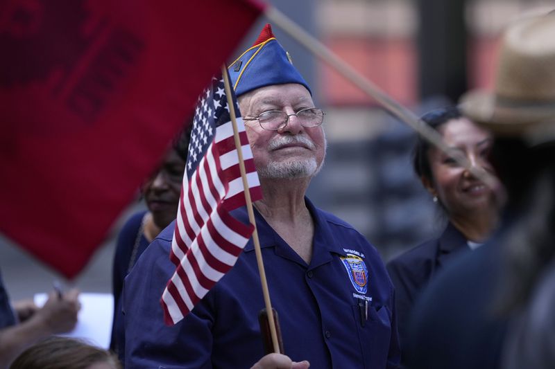 Roman Rena waves a flag at a news conference where Officials with the League of United Latin American Citizens, or LULAC, held a news conference to respond to allegations by Texas Attorney General Ken Paxton, Monday, Aug. 26, 2024, in San Antonio. (AP Photo/Eric Gay)