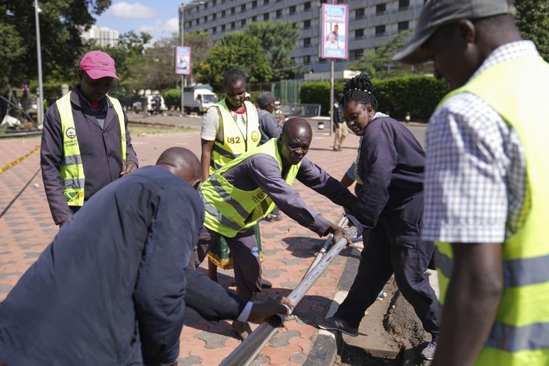 Nairobi county workers repair a road barrier in downtown Nairobi, Kenya, Wednesday, June 26, 2024. Thousands of protesters stormed and burned a section of Kenya's parliament Tuesday to protest tax proposals. Police responded with gunfire and several protesters were killed. (AP Photo/Brian Inganga)