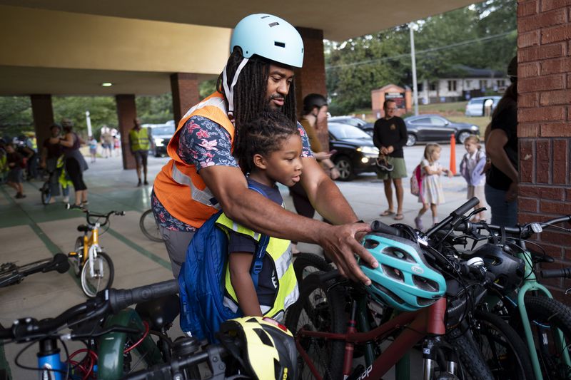 David Franklin helps hang is son Dawson’s helmet after the pair rode with the weekly Parkside Elementary School “bike bus” Friday, Sept. 20, 2024, in Atlanta. Ben Gray for the Atlanta Journal-Constitution