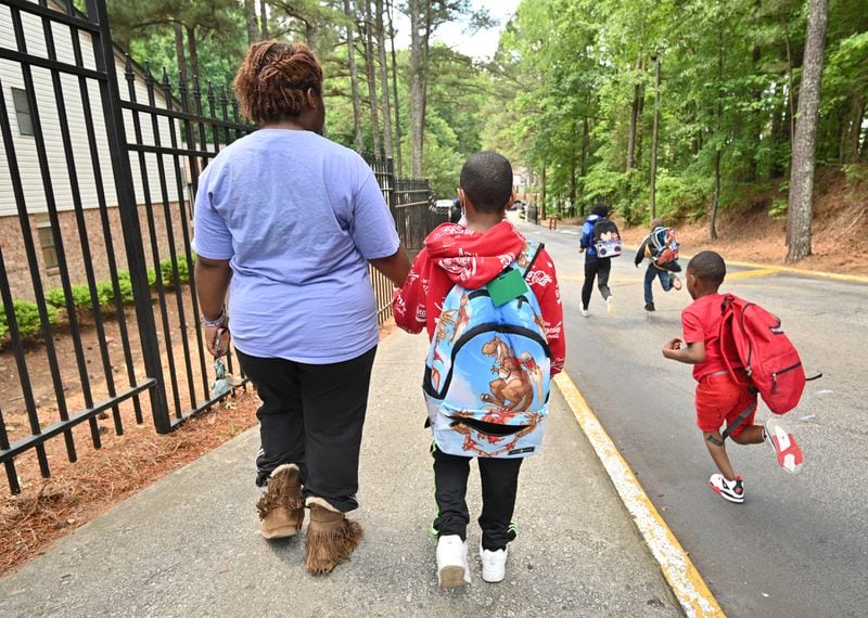 Alexis Cargile, a resident at the apartment complex formerly known as The Life at Greenbriar, walks her 7-year-old son, Logan, home from the school bus stop in May. Cargile says that shootings at the complex have made life there unsuitable for raising children. “There is no way — no way — that kids should have to live like this,” she says. (Hyosub Shin / Hyosub.Shin@ajc.com)