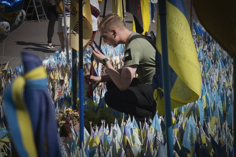 A veteran holds a photo if his comrade at a makeshift memorial for fallen Ukrainian soldiers in Russian-Ukrainian war during Ukrainian Independence Day on Independence Square in Kyiv, Ukraine, Saturday, Aug. 24, 2024. (AP Photo/Efrem Lukatsky)