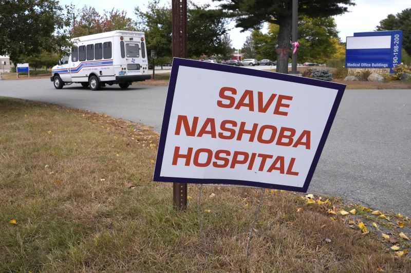 A senior shuttle bus going to a nearby retirement home rolls past a "Save Nashoba Hospital" sign displayed outside the former Nashoba Valley Medical Center, which closed on Aug. 31, 2024 and was part of the bankrupt Steward Health Care company, Thursday, Sept. 19, 2024, in Ayer, Mass. (AP Photo/Charles Krupa)