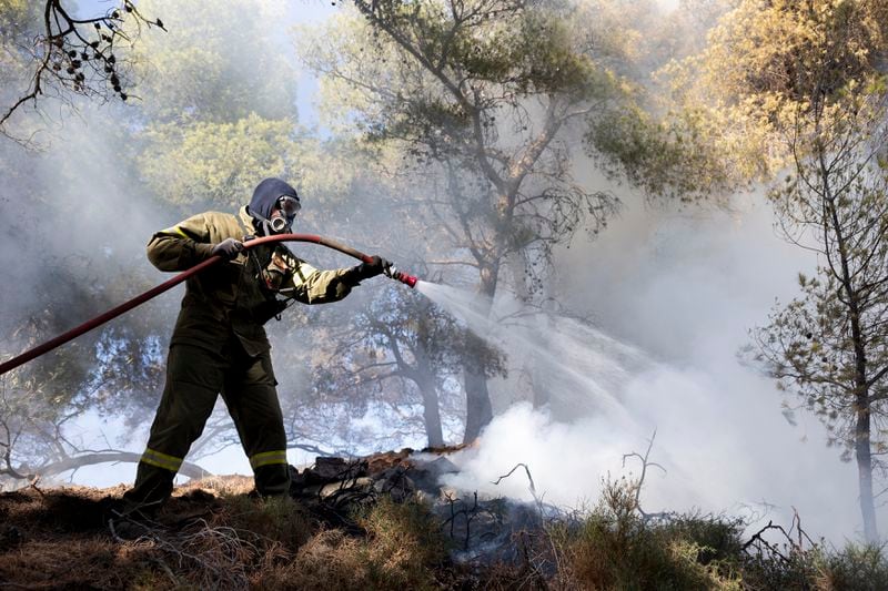 A firefighter struggles to extinguish a forest fire in the Keratea area, southeast of Athens, Greece, Sunday, June 30, 2024. Two large wildfires were burning Sunday near Greece's capital of Athens, and authorities sent emergency messages for some residents to evacuate and others to stay at home and close their windows to protect themselves from smoke. (AP Photo/Yorgos Karahalis)