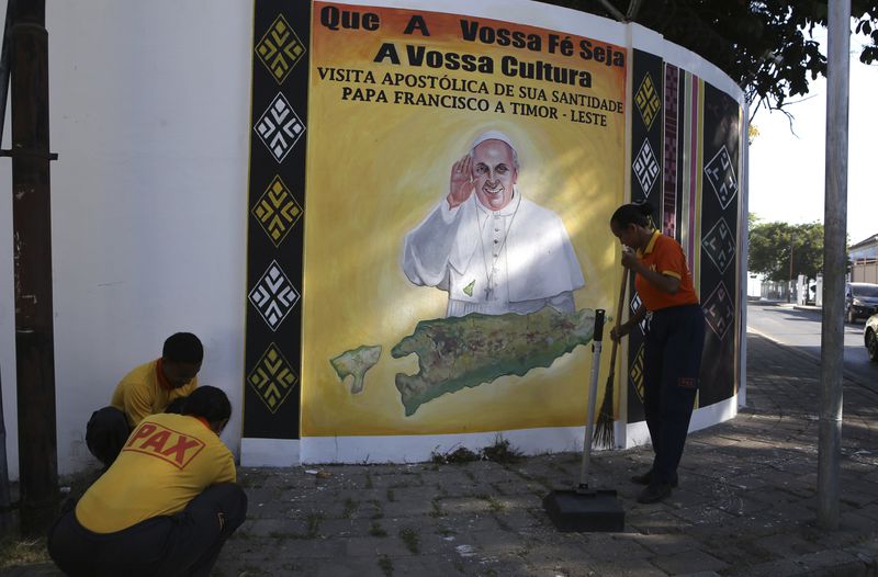 People clean a street next to a banner welcoming Pope Francis in Dili, East Timor Friday, Sept. 6, 2024. (AP Photo/Firdia Lisnawati)