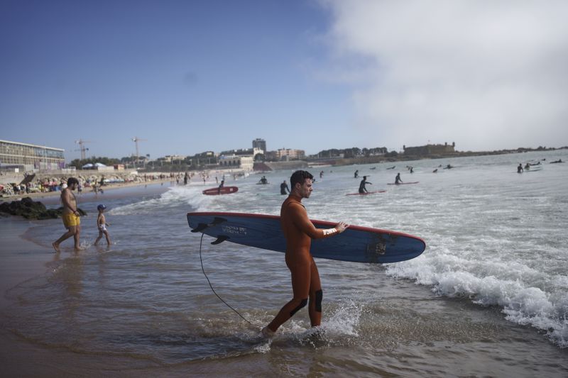 Surf Church's pastor, the Rev. Samuel Cianelli, walks into the Atlantic Ocean to surf with his congregation in Matosinhos beach in the suburbs of Porto, Portugal on Sunday, Aug. 18, 2024. (AP Photo/Luis Andres Henao)