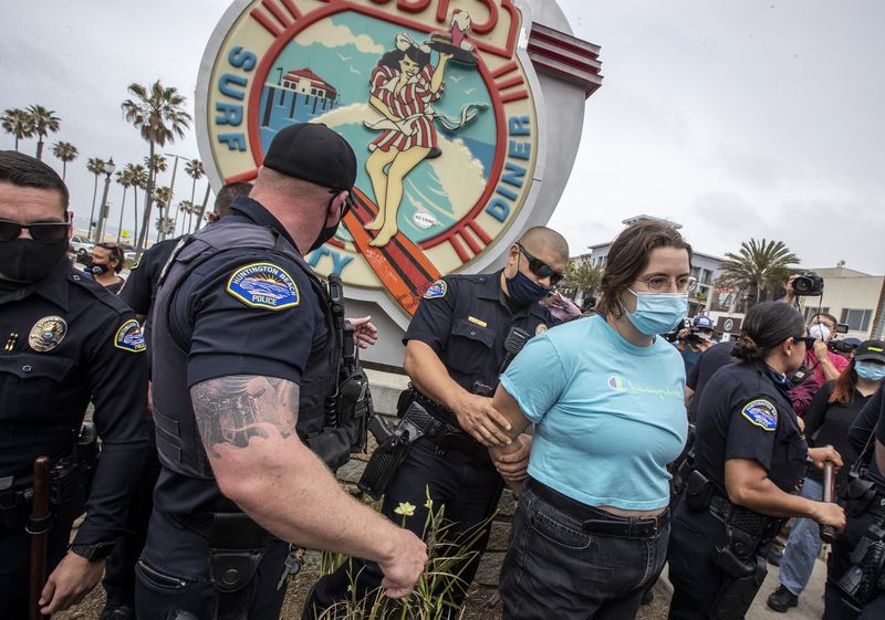 Huntington Beach police officers arrest a woman for allegedly possessing pepper spray as protesters gathered to demonstrate against a so-called White Lives Matter rally Sunday in Huntington Beach, California.