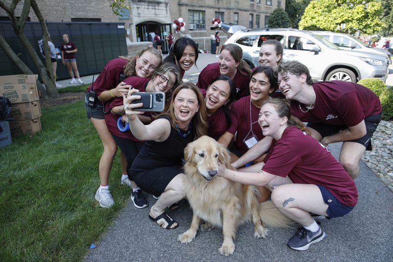 Tania Tetlow, president of Fordham University, holds her dog Archie as she poses with students during Move In Day at the Bronx campus, Sunday, Aug. 25, 2024, in New York. (AP Photo/Kena Betancur)