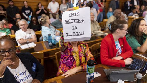 An attendee holds a sign that says "This Meeting is Illegal" during a hastily planned State Election Board meeting at the Capitol in Atlanta on Friday. Votes taken at that meeting have spurred threats of litigation, as well as a request to the governor to remove the board members and executive director who took part in the meeting. (Arvin Temkar/Atlanta Journal-Constitution via AP)
