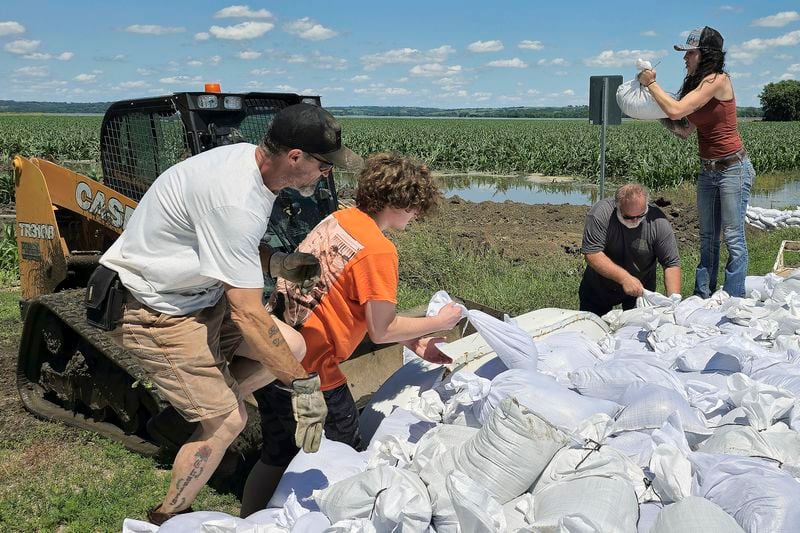 Volunteers toss sandbags into the bucket of a loader that will take them to be used to reinforce a berm on the northeast side of Jefferson, South Dakota, Sunday, June 23, 2024. The sandbag effort is an attempt to keep floodwaters from the Big Sioux River from inundating the town. (Tim Hynds/Sioux City Journal via AP)
