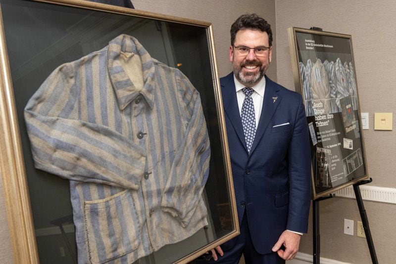 Dr. Reuben Sloan stands with a prison jacket similar to what his father, Icek Slodowski aka Erving Sloan, would have worn in a WWII concentration camp. Phil Skinner for The Atlanta Journal-Constitution