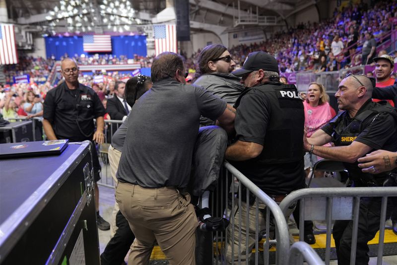 Police remove a man, center with sunglasses, who had climbed onto the media riser, as Republican presidential nominee former President Donald Trump speaks at a campaign event, Friday, Aug. 30, 2024, in Johnstown, Pa. (AP Photo/Alex Brandon)