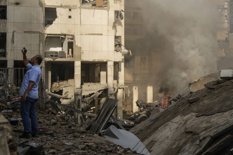 A man documents the damaged buildings at the site of an Israeli airstrike in Beirut's southern suburb, Lebanon, Tuesday, Oct. 1, 2024. (AP Photo/Hassan Ammar)