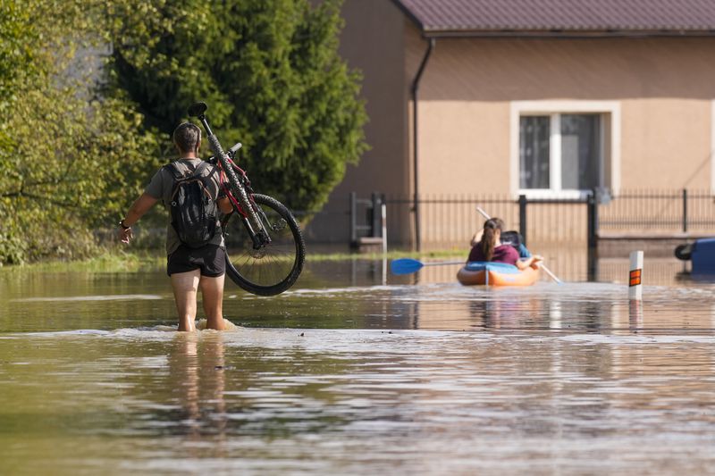 A resident carries his bicycle as others paddle through a flooded street in Bohumin, Czech Republic, Tuesday, Sept. 17, 2024. (AP Photo/Darko Bandic)