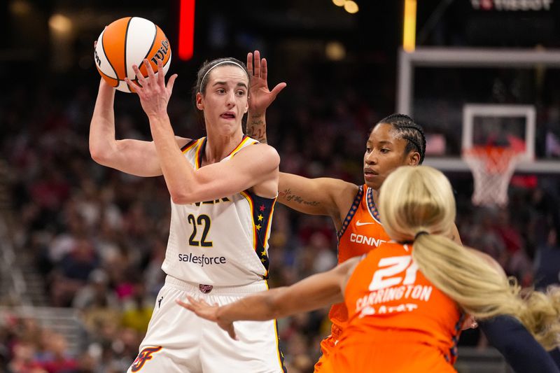 Indiana Fever guard Caitlin Clark (22) looks to pass over Connecticut Sun guard Tyasha Harris (52) and guard DiJonai Carrington (21) in the second half of a WNBA basketball game in Indianapolis, Monday, May 20, 2024. (AP Photo/Michael Conroy)