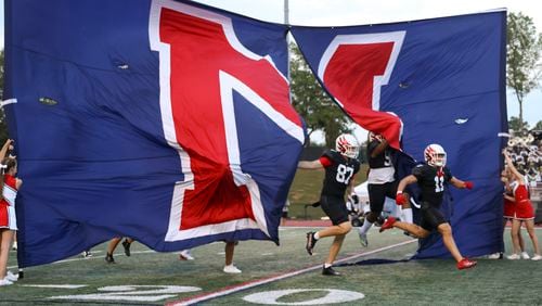 Milton players run through the school’s banner before their game against Buford at Milton High School, Friday, August 16, 2024, in Milton, Ga. (Jason Getz / AJC)
