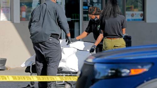 A body is removed from the scene of a shooting in the parking lot of a Chevron station Wednesday morning. Police later arrested a rideshare driver on a murder charge.