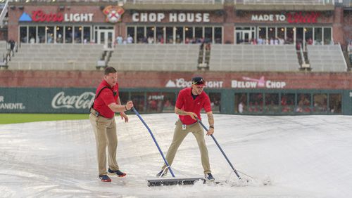Field staff push rainwater off of a tarp over the infield during the rain delay of a baseball game between the Atlanta Braves and the St. Louis Cardinals, Friday, July 19, 2024, in Atlanta. (AP Photo/Jason Allen)