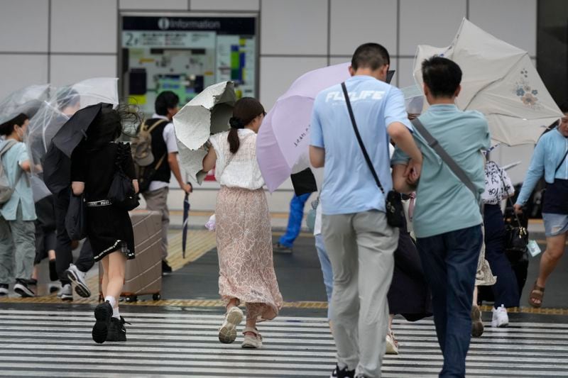 People holding umbrellas walk along a street, in the strong wind as Typhoon Ampil approaches the Tokyo area, Japan, Friday, Aug. 16, 2024. (AP Photo/Hiro Komae)