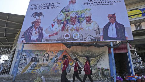 A billboard welcoming Pope Francis stands above a mural honoring Bishop Belo and three others as national heros in Dili, East Timor, Wednesday, Aug. 14, 2024. (AP Photo/Achmad Ibrahim)