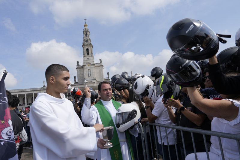 A priest holding a police motorcycling helmet, blesses the helmets of faithful during the IX Pilgrimage of the Blessing of Helmets that draws tens of thousands at the Roman Catholic holy shrine of Fatima, in Fatima, Portugal, Sunday, Sept. 22, 2024. (AP Photo/Ana Brigida)