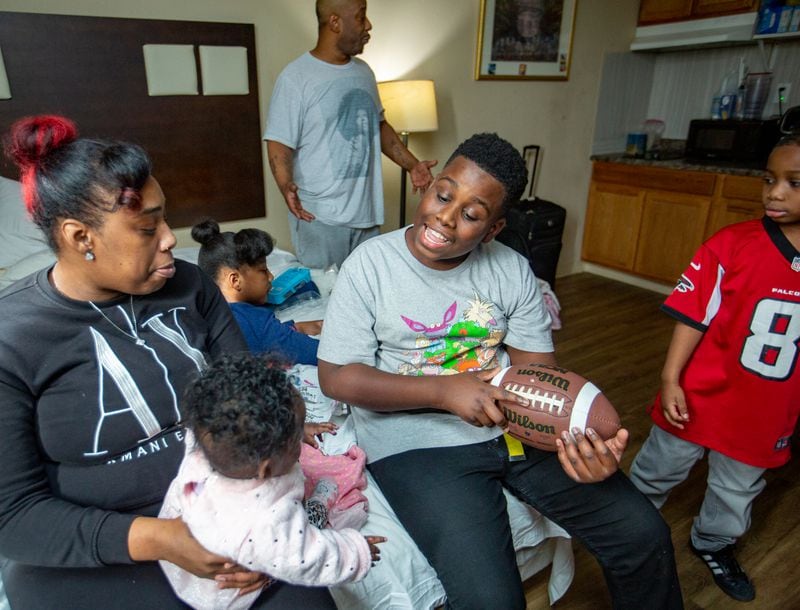 The White family lives in an extended-stay hotel where parents Raneice, left, and Melvin, standing back, live with five of their children including 5 month-old Justice, from left, Mckenzie, 10, blue shirt on bed; Money, 13, with football and King, 7, right, on Wednesday, Dec 21, 2022.  The family has lived in extended-stay hotels for years.  Despite Melvin working full-time, they canÕt find long-term safe housing they can afford.  (Jenni Girtman for The Atlanta Journal-Constitution)