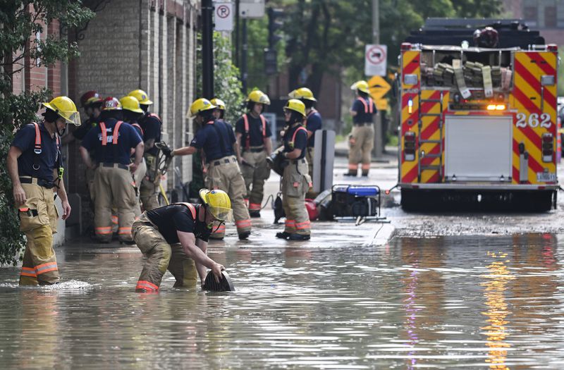 Firefighters remove a manhole cover following a water main break on a street in Montreal, Friday, Aug. 16, 2024, causing flooding in several streets of the area. (Graham Hughes/The Canadian Press via AP)