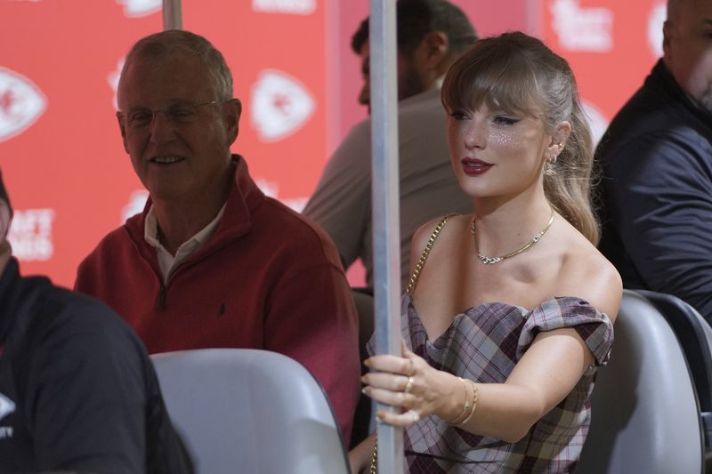 Taylor Swift arrives in a cart with her dad, Scott Swift, left, before the start of an NFL football game between the Kansas City Chiefs and the New Orleans Saints Monday, Oct. 7, 2024, in Kansas City, Mo. (AP Photo/Charlie Riedel)