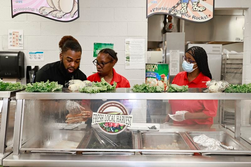 (Left to right) Cafeteria manager Montavious Jenkins prepares lunch for students along with food assistants Rosa Burley and Barbara Watson at Burgess-Peterson Academy in Atlanta on Thursday, Aug. 4, 2022. (Natrice Miller/natrice.miller@ajc.com)
